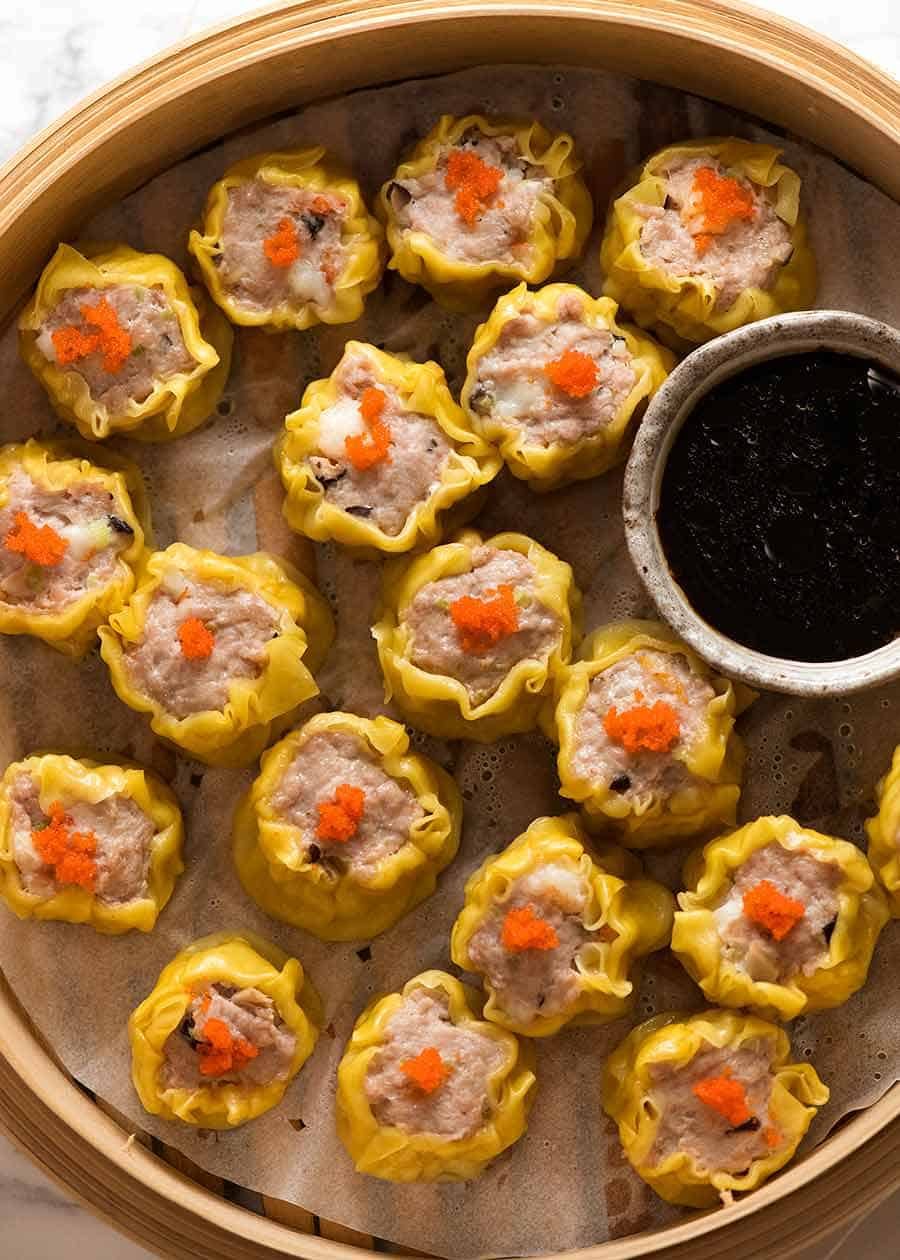 Overhead photo of Siu Mai (Chinese steamed dumpling) dipped in sauce in a bamboo steamer