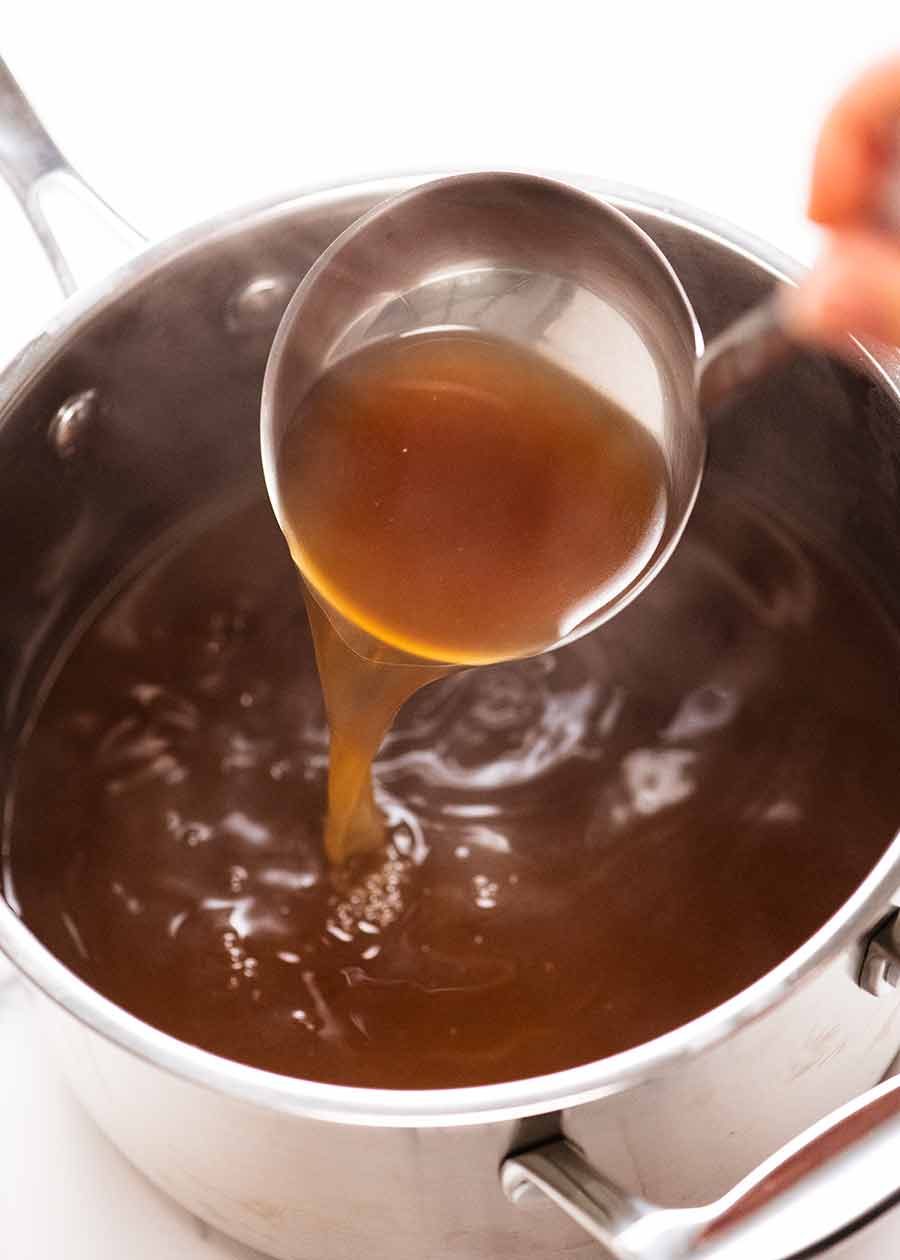 Ladle scooping up hot beef stock from pot